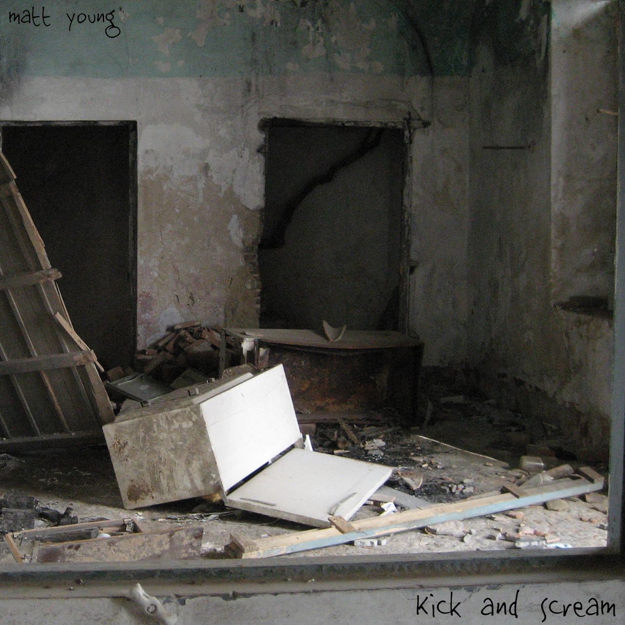 A room in an abandoned house scattered with debris including an open refrigerator lying on its side and bits of broken wood.